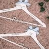Perchas de madera personalizadas para novios en color blanco con nombres grabados Mariángeles y Javier, fecha de boda 1 de Agosto de 2026, lazos azul celeste y frase Un sí para toda la vida, creadas por Aura's Personality