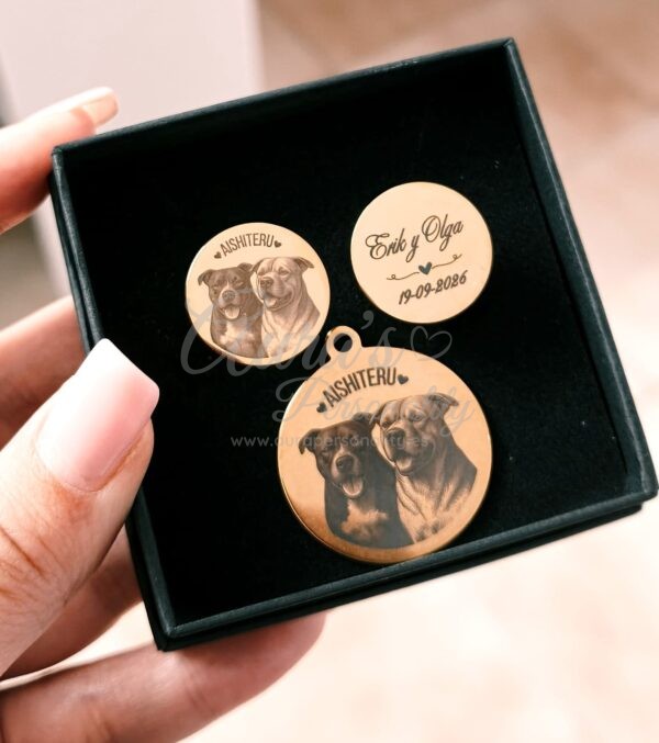 Mano sosteniendo una caja de joyería negra de Aura's Personality con un set promocional dorado a juego de gemelos de 2cm y medalla de ramo de 3cm grabados con foto de dos perros y texto Aishiteru Erik y Olga 19-09-2026