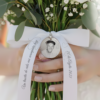 Lazo de raso blanco personalizado en ramo de novia, sosteniendo medalla de recuerdo grabada.