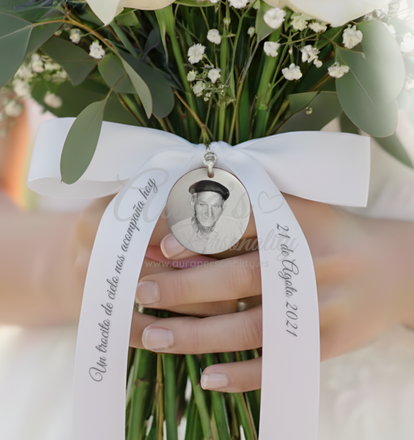 Lazo de raso blanco personalizado en ramo de novia, sosteniendo medalla de recuerdo grabada.